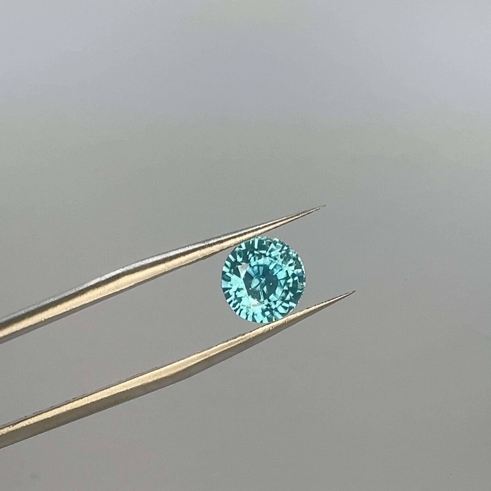 round blue zircon held by tweezers