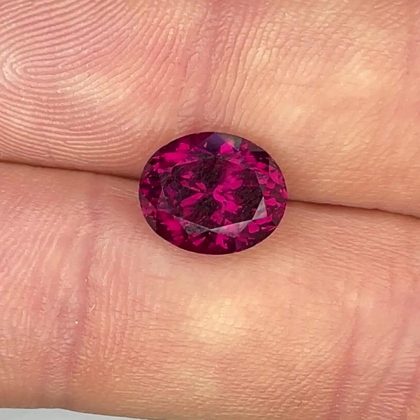 Raspberry red rhodolite oval garnet macro in between fingers