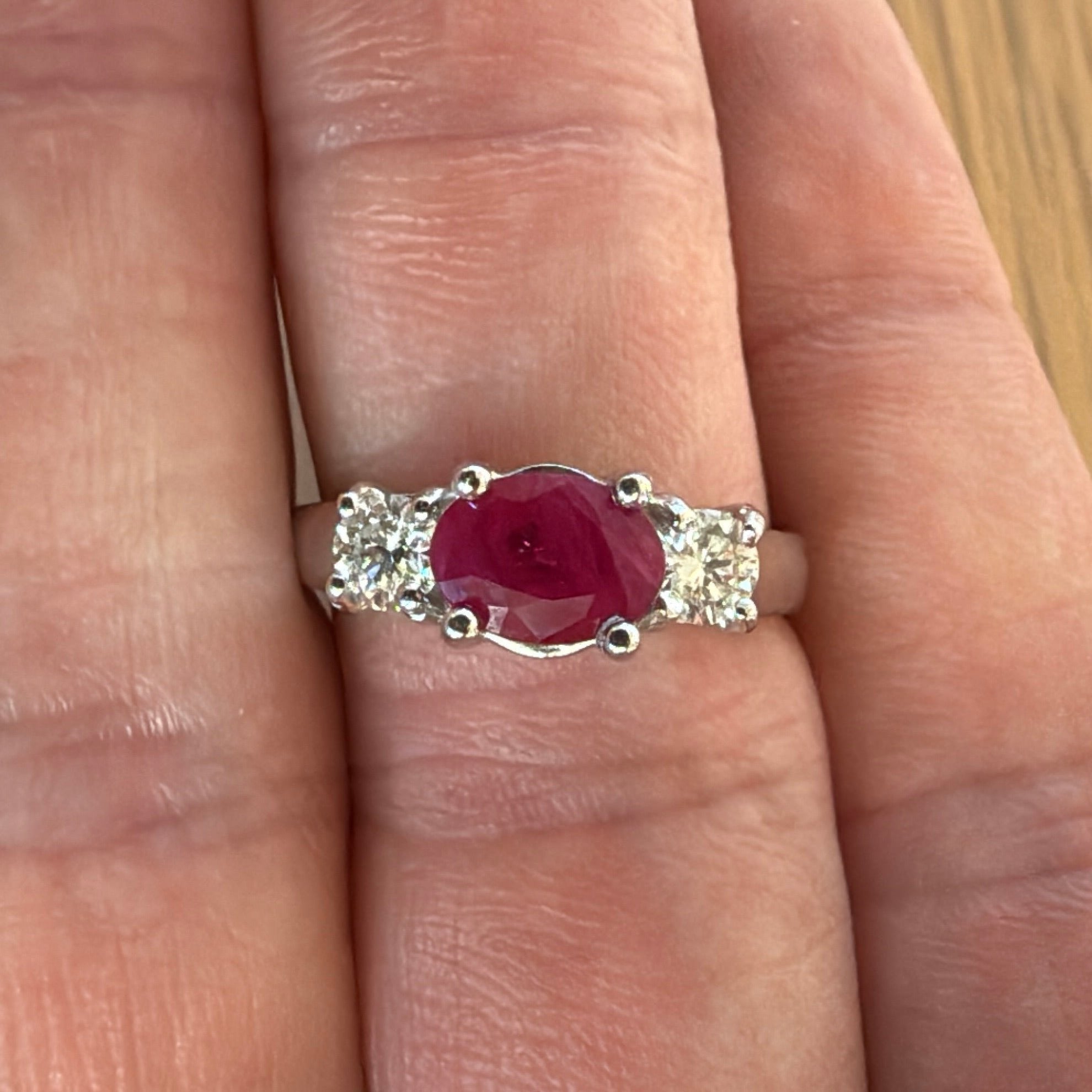 ruby three stone ring with 2 round accent diamonds. Red oval ruby east west in white gold